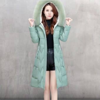 Vrouw draagt een blauwe donsjas met capuchon over haar hoofd tegen een betongrijze achtergrond.