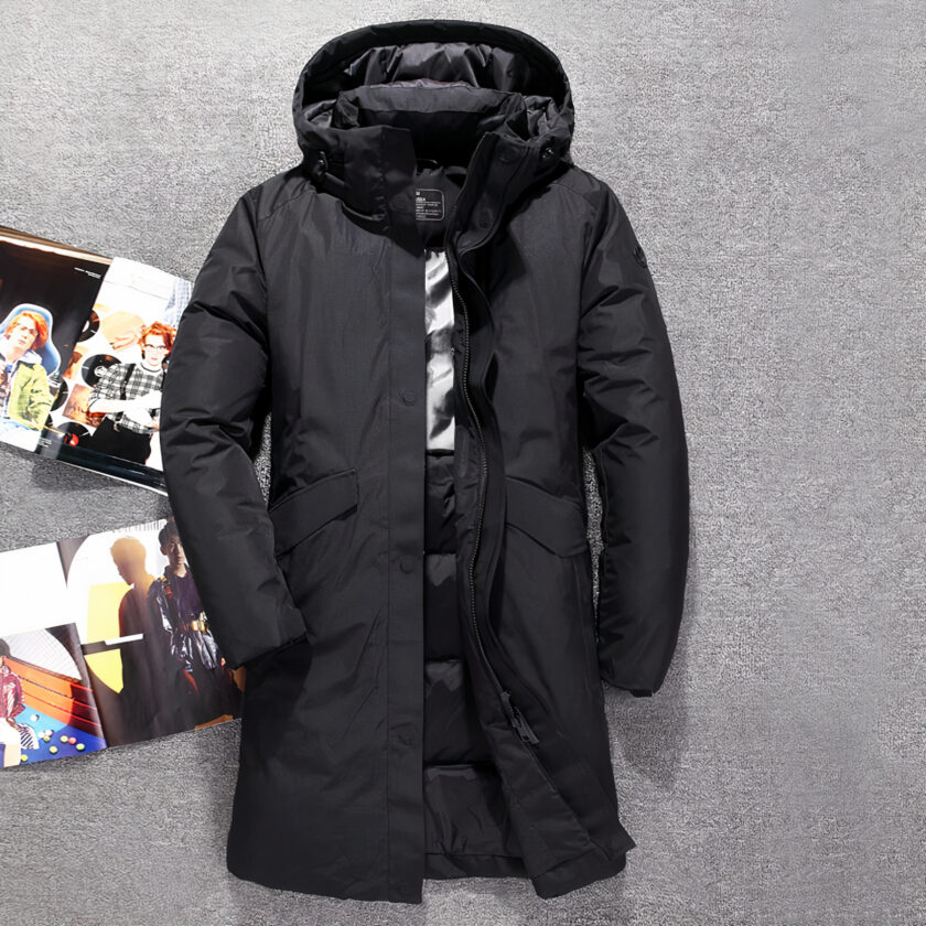 Donsjack voor heren, lang en dik Lange, zwarte donsjas met capuchon op een grijze achtergrond.