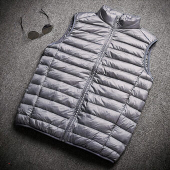 Grijs mouwloos donsjack op een grijze vloer met een zonnebril ernaast