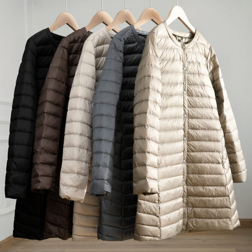 5 lichte en lange donsjassen in wit, grijs, zwart en bruin hingen op hangers.