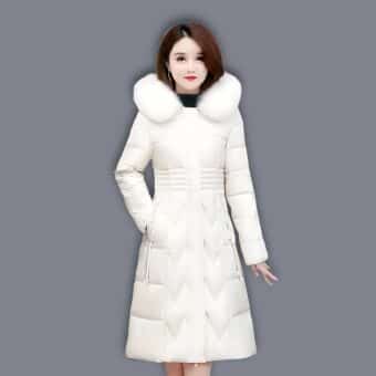 Bruine Aziatische vrouw draagt een lange, gewatteerde witte donsjas met bontkraag. Haar rechterhand in de zak van de donsjas. Grijze achtergrond.