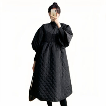 We zien een donkerharige vrouw in een nette zwarte jas met een gewatteerde omslagkraag. Ze neemt een foto van zichzelf en we kunnen haar gezicht niet zien. De achtergrond is wit.