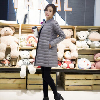 Vrouw poseert voor een pluche plank en draagt een zwarte broek en een grijs donsjack.