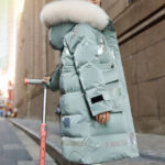 Tienermeisje op een scooter in de straat met een groene donsjas en witte bontmuts.