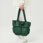 Een vrouwenbeen in profiel met witte broek op een witte achtergrond, met een grote groene gewatteerde plunjezak met een geïntegreerde schouderriem.