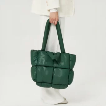 Een vrouwenbeen in profiel met witte broek op een witte achtergrond, met een grote groene gewatteerde plunjezak met een geïntegreerde schouderriem.