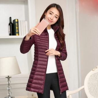 Vrouw met een bordeauxrode donsjas die een foto van zichzelf maakt met haar mobiele telefoon, met daarachter een lamp en een plank.