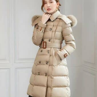 Aziatische vrouw met achterover gebonden haar, draagt een getailleerd, halflang donsjack met een bontkraag. Haar linkerhand zit in de zak van het donsjack, haar rechterhand op de kraag. De muren zijn wit.