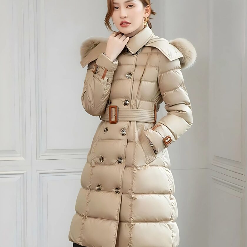 Aziatische vrouw met achterover gebonden haar, draagt een getailleerd, halflang donsjack met een bontkraag. Haar linkerhand zit in de zak van het donsjack, haar rechterhand op de kraag. De muren zijn wit.