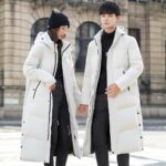 Lange uniseks zwarte of witte donsjas gedragen door een jonge man en een jonge vrouw in een besneeuwde straat