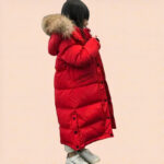 Klein meisje dat een rood kinderdonsjack met capuchon draagt op een roze achtergrond.