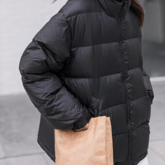 foto van een vrouw in een kort zwart donsjack die over straat loopt