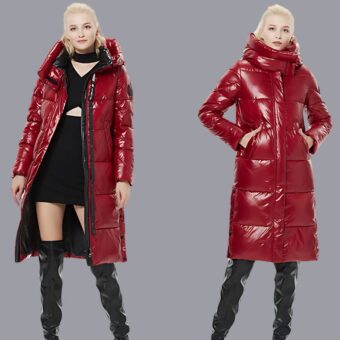 Een jonge blonde vrouw draagt een lang, gewatteerd, rood gelakt donsjack, links open en rechts dicht en met haar handen in haar zakken, tegen een roomwitte achtergrond.