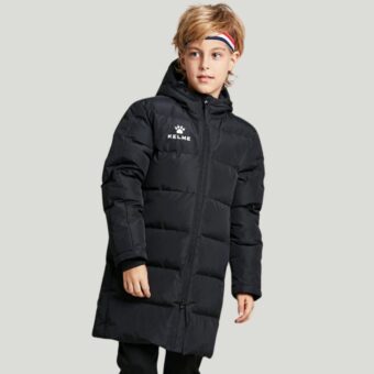 Een jonge blonde jongen draagt een lang gewatteerd katoenen sportjack voor kinderen en poseert voor een grijze achtergrond.