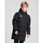 Een jongen tegen een grijze achtergrond met een lange zwarte gewatteerde donsjas met capuchon en een driekleurige hoofdband in de kleuren van de Franse vlag in zijn lichtbruine haar.