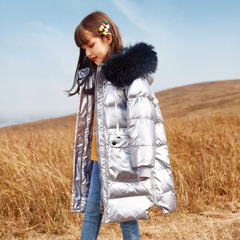 Lange grijze donsjas met bontmuts gedragen door een brunette tiener in een veld.