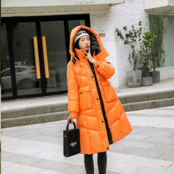 Vrouw draagt een oranje donsjack en houdt een zwarte handtas vast, staande op straat.