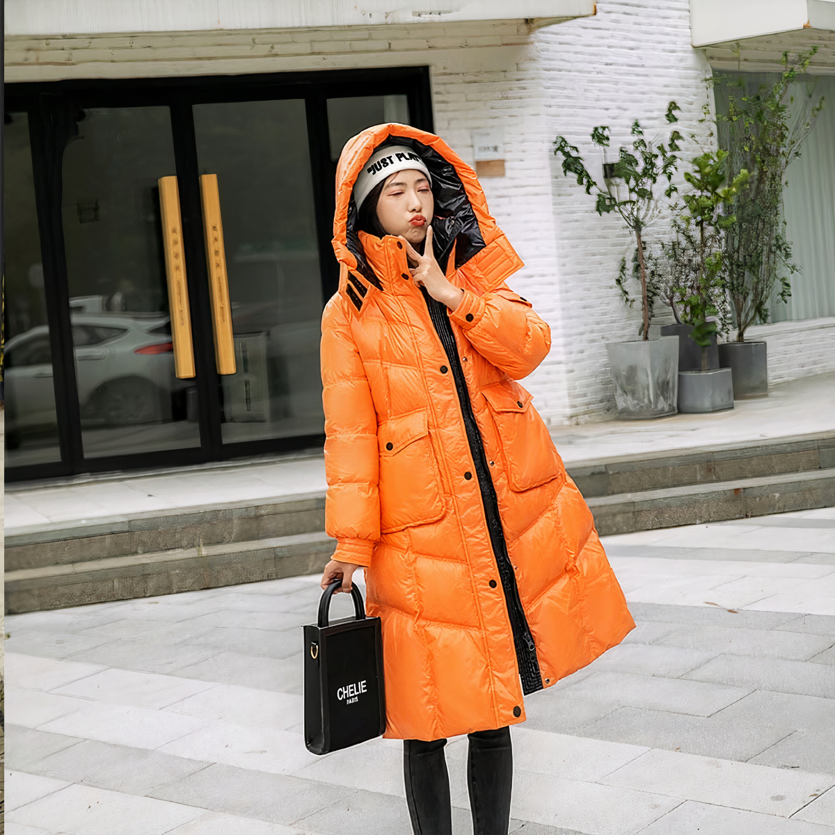 Vrouw draagt een oranje donsjack en houdt een zwarte handtas vast, staande op straat.