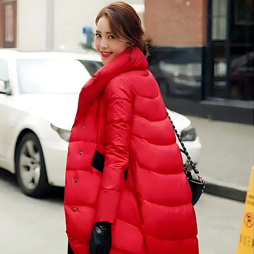 Foto van een vrouw in een lange rode donsjas die over straat loopt, met linksachter een witte auto en rechtsachter een gele bink.