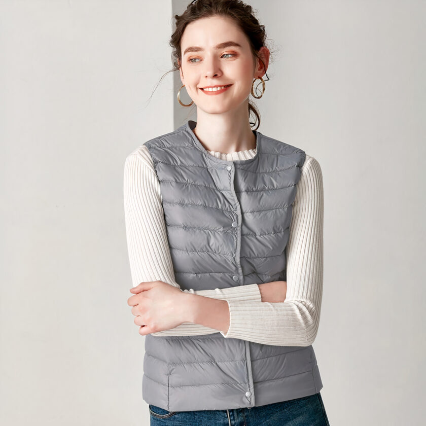 Vrouw met haar armen over elkaar, draagt een witte top met lange mouwen en een grijs mouwloos donsjack.