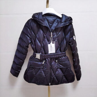 Het jack is zwart, gewatteerd en heeft een riem, een slanke pasvorm, een getailleerd model en een capuchon. Het wordt gepresenteerd op een hangende riem, tegen een grijze achtergrond. Het label is bevestigd aan de ritssluiting.