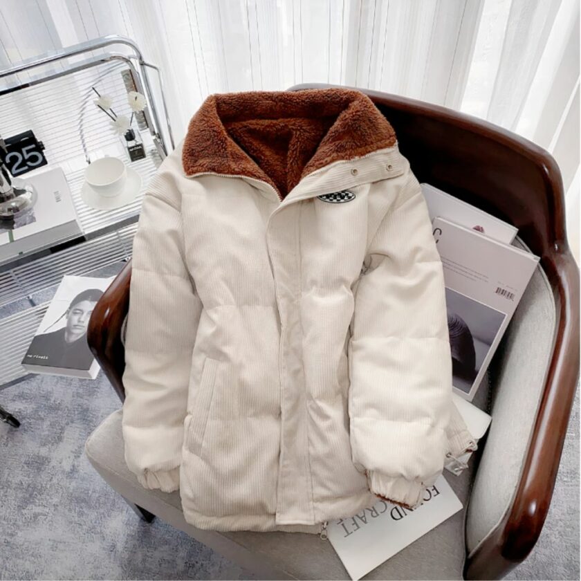 Een wit heren corduroy donsjack met een bruine fleece voering zit op een bank in een mannelijke kamer.