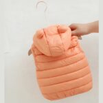 Dit is een mouwloos donsjack met capuchon, zalmkleurig en gewatteerd.