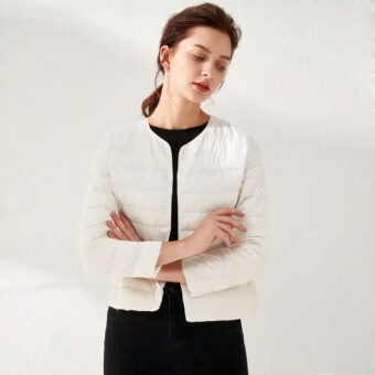 Vrouw die een witte donsjas draagt en haar armen kruist, witte achtergrond.