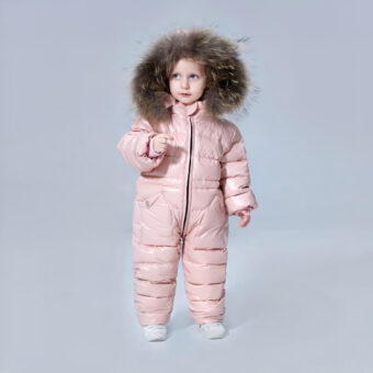 Klein meisje dat een roze donsjack met volledige bescherming draagt met de capuchon over haar hoofd voor een grijze achtergrond.