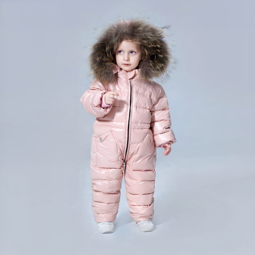 Klein meisje dat een roze donsjack met volledige bescherming draagt met de capuchon over haar hoofd voor een grijze achtergrond.