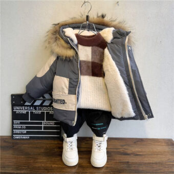 Een warme, dikke katoenen jas aan een kleerhanger tegen een grijze muur, parketvloer en witte schoenen op de vloer.