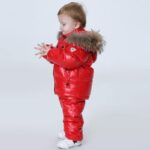 Kleine jongen op een grijze achtergrond die een rode warme winterdonsjas draagt.