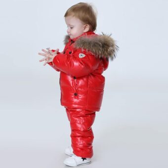 Kleine jongen op een grijze achtergrond die een rode warme winterdonsjas draagt.