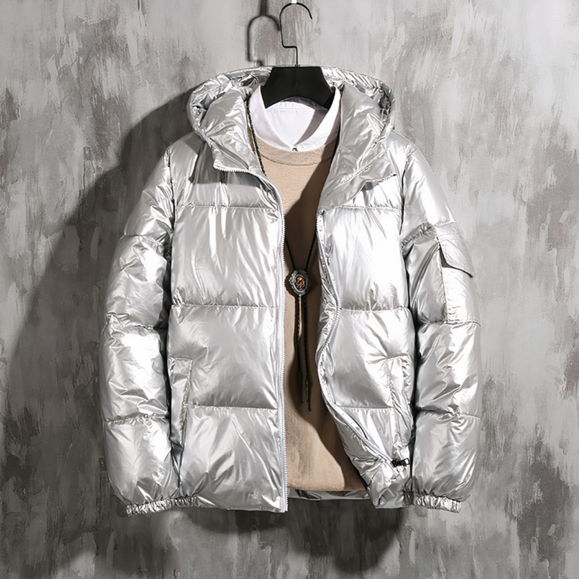 Zilveren jas voor heren Foto van een zilveren donsjack van een man op een hanger voor een gewaxte betonnen muur, gedragen met een beige trui en een wit overhemd.