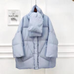 Het oversized lichtblauwe donsjack wordt gepresenteerd tegen een lichte, minimalistische achtergrond.
