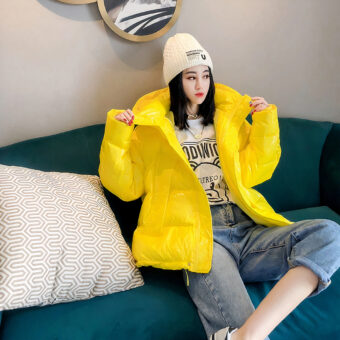 Vrouw met gele jas en beige muts zittend op een groene sofa met een groot beige kussen en een spiegel achter haar