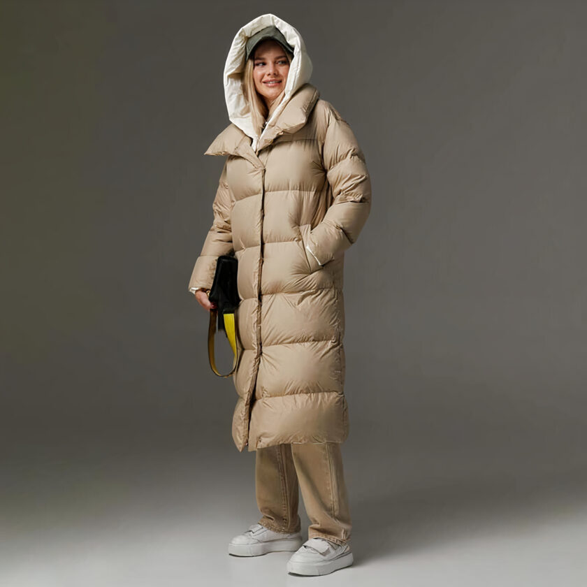 Foto van een vrouw met een lange kaki donsjas tegen een donkere achtergrond