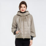 Bruine vrouw tegen een grijze achtergrond die een grote beige donsjack draagt.