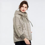 Bruine vrouw tegen een grijze achtergrond die een grote beige donsjack draagt.