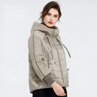 Bruine vrouw tegen een grijze achtergrond die een grote beige donsjack draagt.