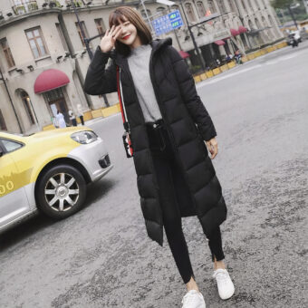 Vrouw op straat met een lange zwarte donsjas. Gele auto aan de linkerkant.