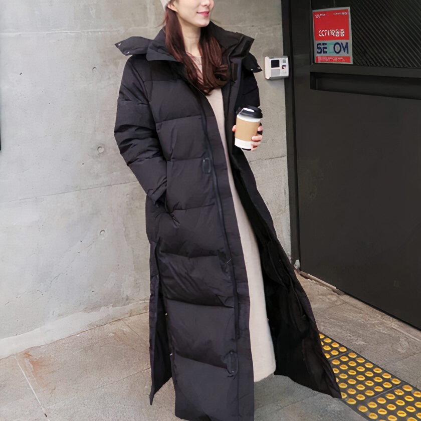 Bruinharige vrouw in een trappenhuis, voor een nooddeur, met een grote, warme, zwarte donsjack met capuchon.