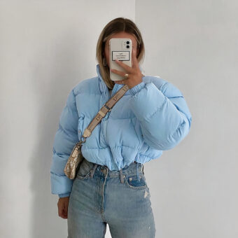 Foto van een vrouw in een kort blauw donsjack die haar gezicht verbergt met haar telefoon