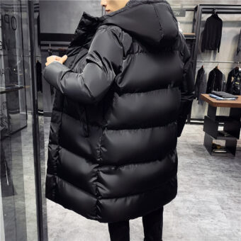 Man staat met zijn rug naar een kamerhoge grijze kledingwinkel en draagt een zwarte parka met capuchon.