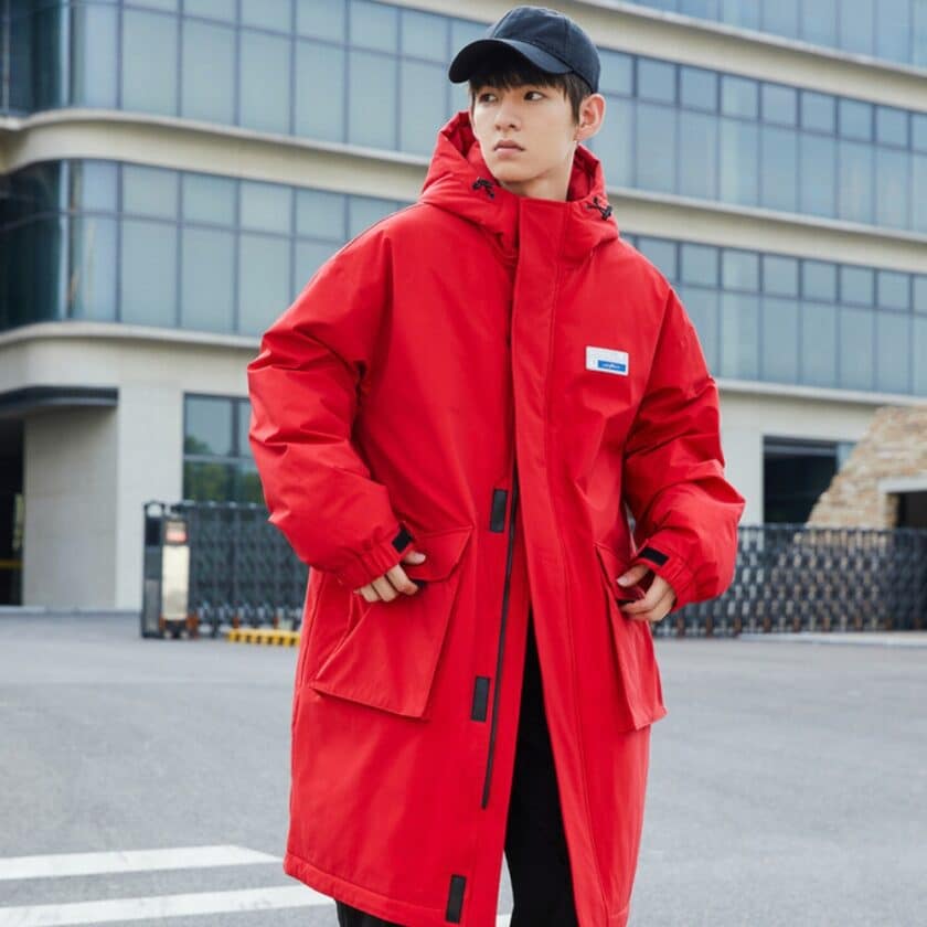 Afbeelding van een man met een rode halflange donsjas en een marineblauwe pet, die op straat staat met zijn handen in de zakken van zijn donsjas.