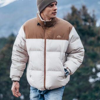 Een man met een wit en bruin donsjack en een muts staat buiten.