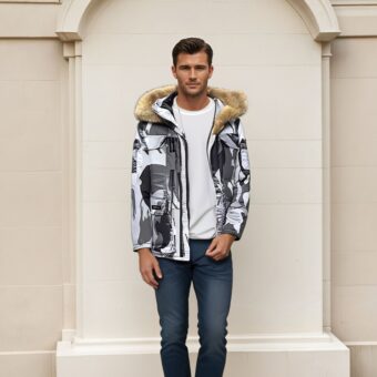 Een man met bruin haar draagt een donkerblauwe spijkerbroek, een wit topje en een donsjack met witte, grijze en zwarte camouflagepatronen en een capuchon van bruin bont. Achter hem een beige stenen muur.