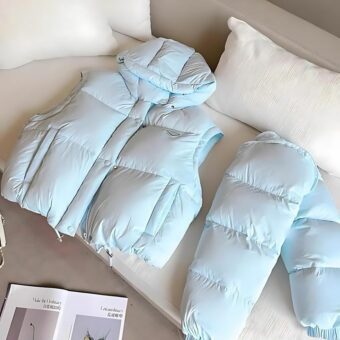 We hebben een hemelsblauw donsjack zonder mouwen op een bank gelegd en nog een donsjack met mouwen, dit keer om te laten zien dat de mouwen van dit donsjack met capuchon afneembaar zijn.