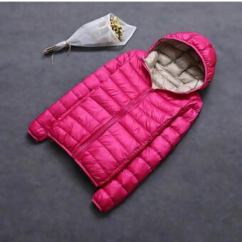 Grote omkeerbare donsjas voor dames in felroze, platgelegd met een beige capuchon, vergezeld van een boeket witte papieren bloemen.