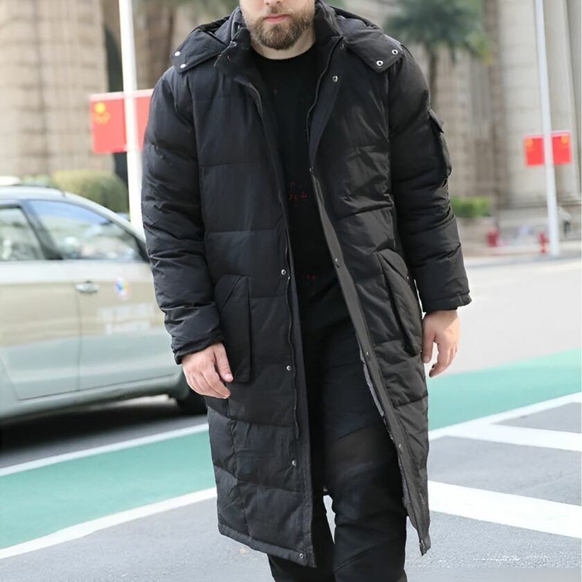Man draagt een grote herenlange donsjas in een straat achter een passerende beige auto.